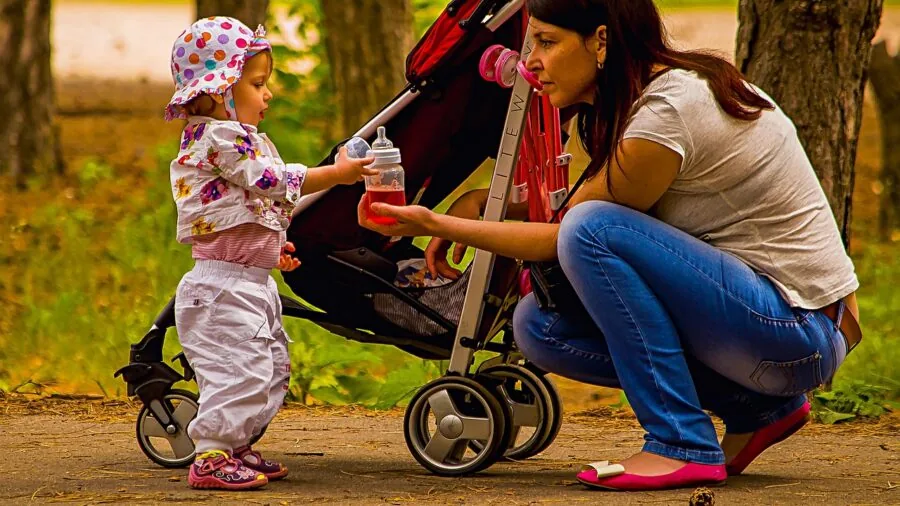 Active parent running outdoors with jogging stroller on park path during daytime