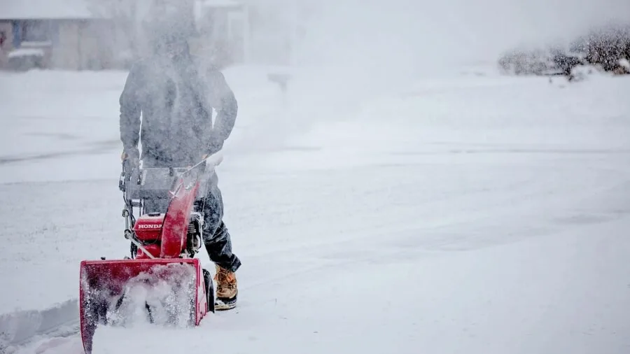 Adult operating a snow blower on a residential driveway during winter weather conditions