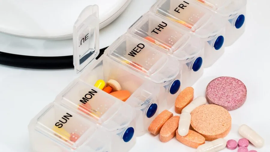 Adult organizing weekly pills in organizer at home kitchen table with natural light
