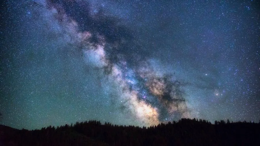 Amateur astronomer looking through telescope at night sky with stars visible overhead
