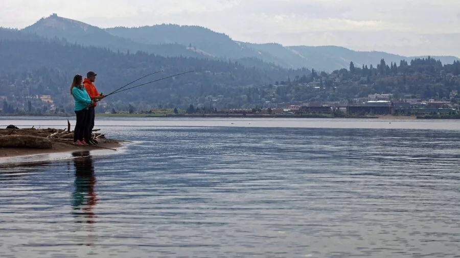 Angler casting fishing line from spinning reel into calm lake water during golden hour