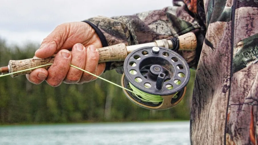 Angler casting fishing line from spinning reel into calm water during daytime fishing session