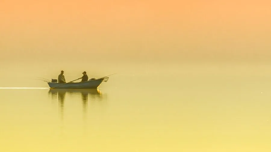 Angler casting line on calm lake at sunrise, focusing on technique and smooth movement