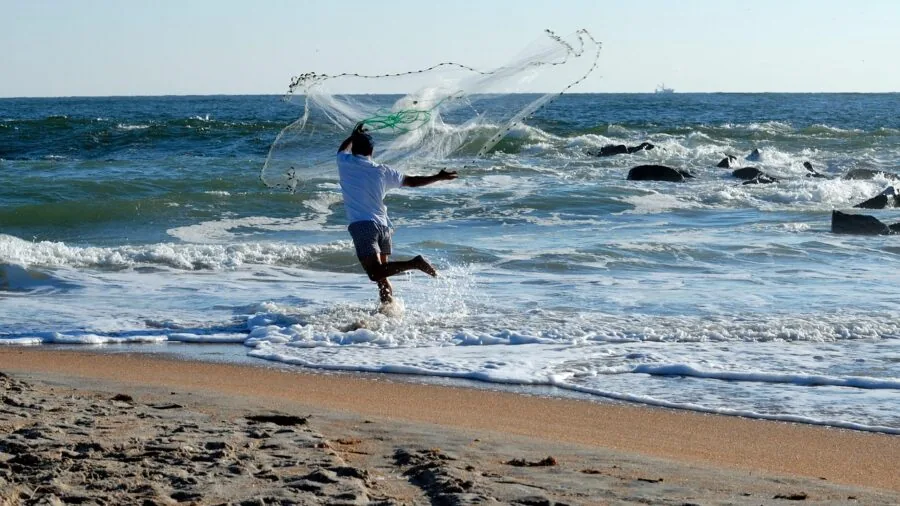 Angler holding extended fishing net while wading in calm water during daytime fishing activity
