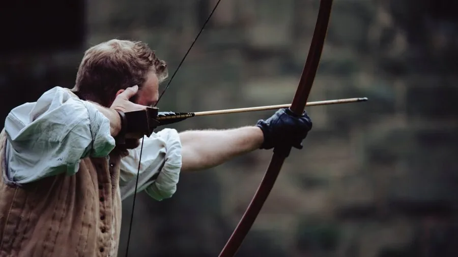 Archer drawing bow while practicing archery in natural outdoor setting during daytime