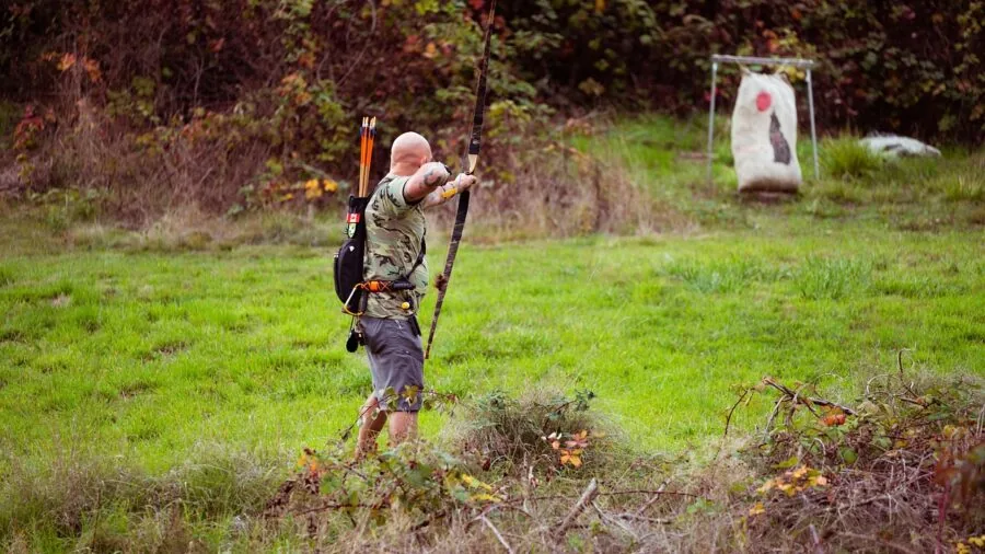 Archer in outdoor setting drawing bow and aiming at archery target in natural daylight