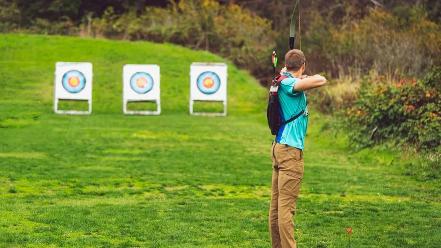 Archer in outdoor setting drawing bow and aiming at distant target with focused concentration