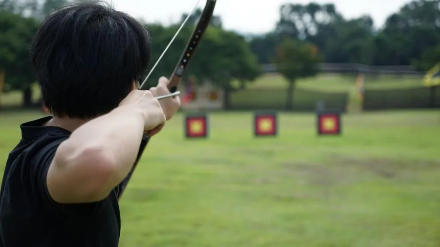 Archer in proper stance drawing compound bow with correct form and posture outdoors