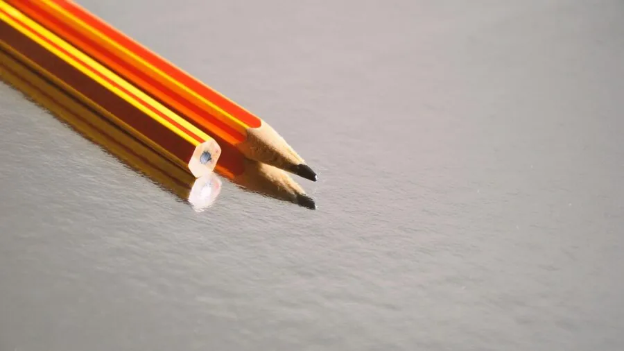 Artist working with graphite pencils on paper at a natural wooden desk with sketches in progress