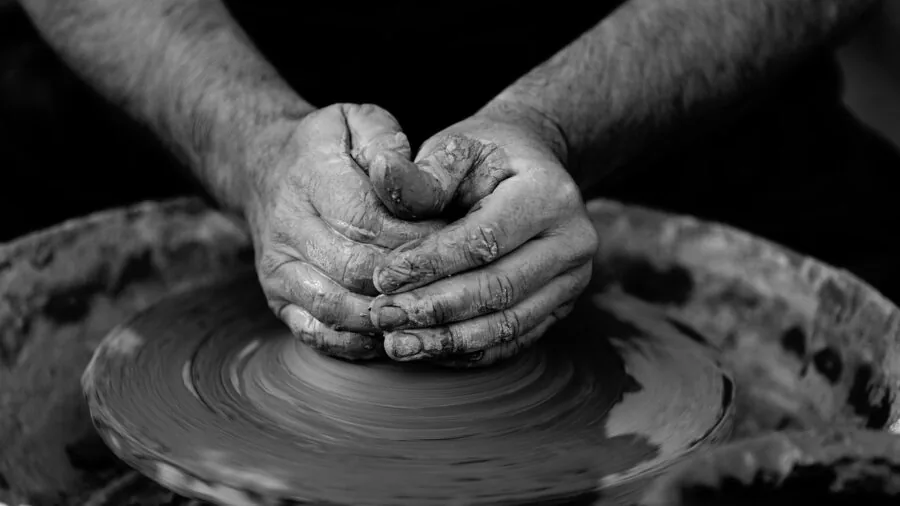 Artist's hands shaping clay on a manual pottery turntable during ceramic work