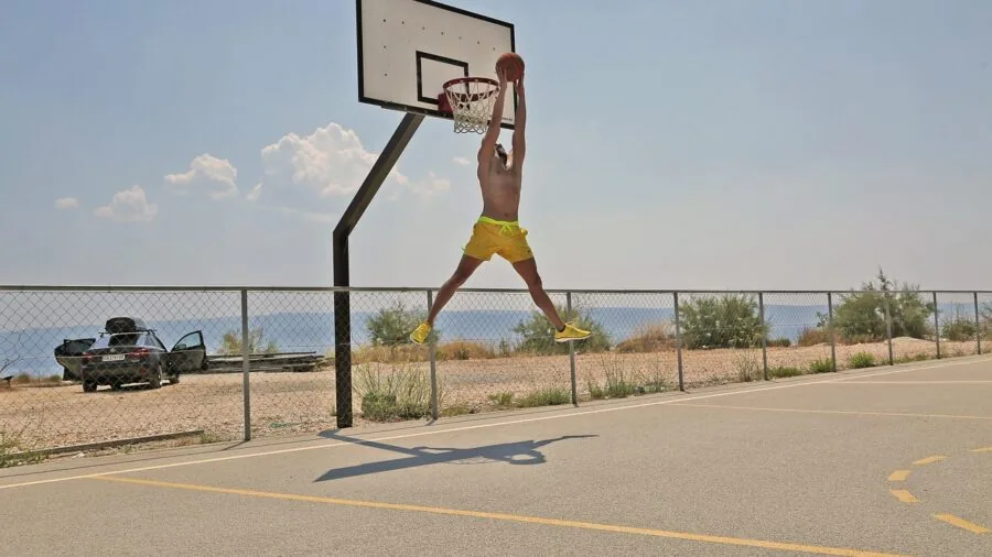Athlete dunking basketball on outdoor court with intense focus and athletic form