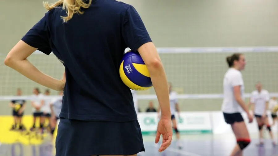 Athletes playing volleyball together on indoor court during practice session