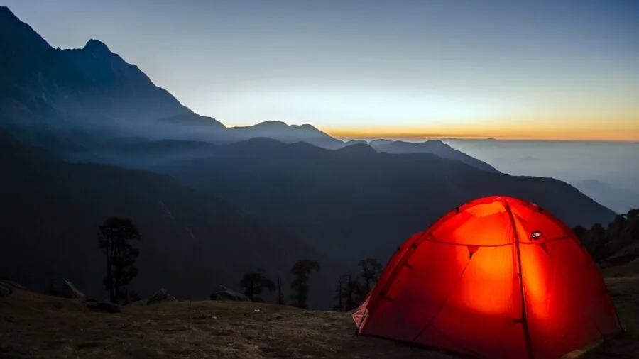 Backpacker setting up camp on a mountain trail at sunset with sleeping gear and tent