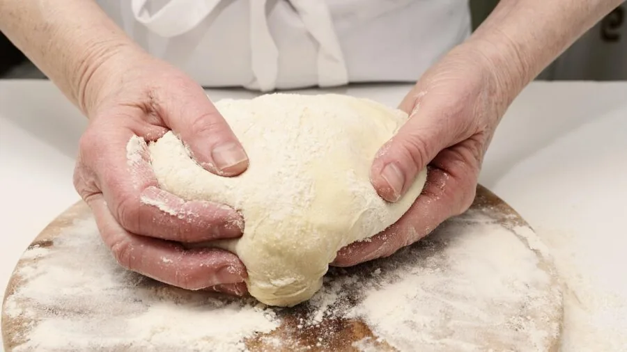 Baker rolling out pastry dough on a work surface in a bright home kitchen