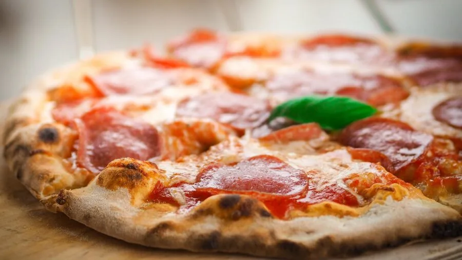 Baker sliding round pizza stone into traditional wood-fired oven for homemade pizza