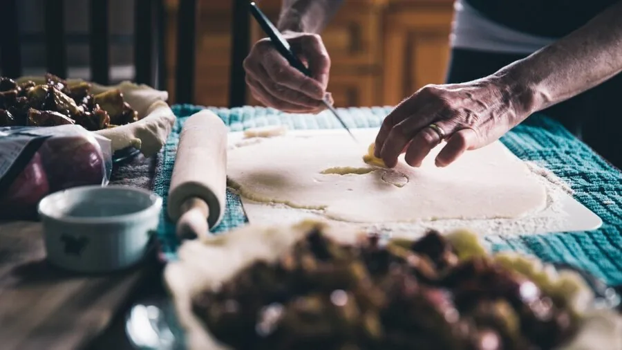 Baker's hands using rolling pin on dough at wooden kitchen counter