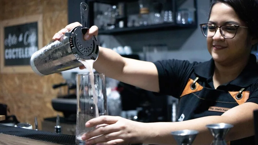 Bartender carefully pouring a mixed cocktail from a shaker into a glass at a bar counter