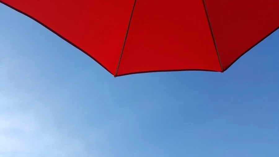 Beach umbrella being tested in strong wind conditions on sandy shore with ocean backdrop