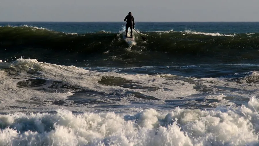 Beginner surfer paddling out on surfboard in ocean waves during golden hour
