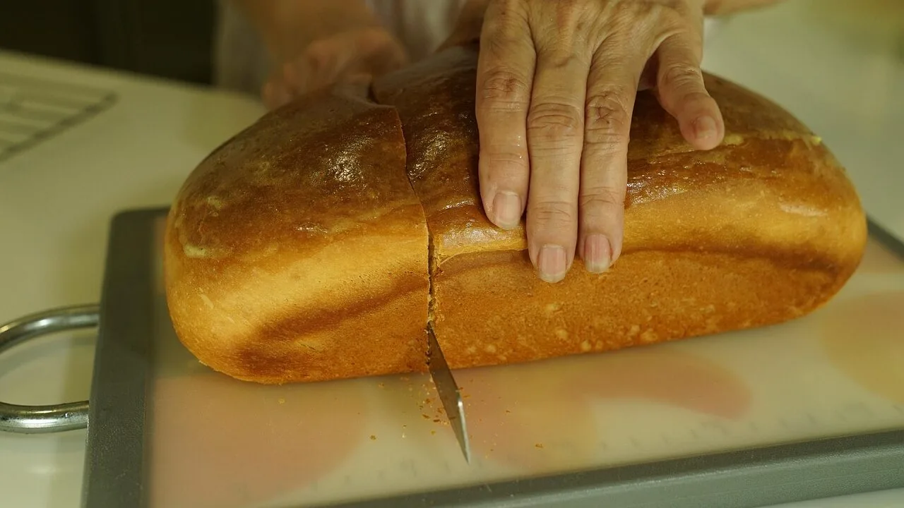 Bread knife with serrated blade cutting through a fresh loaf of bread on wooden cutting board
