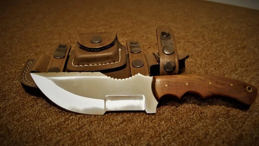 Camper securing knife sheath while preparing outdoor gear in natural wilderness setting