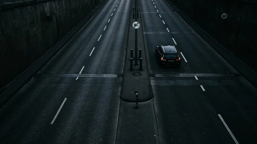 Car being towed on a paved highway with rope or strap visible