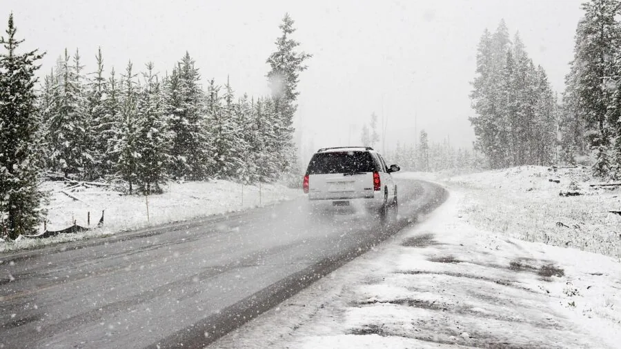 Car driving on snowy winter road with salt spray and harsh weather conditions