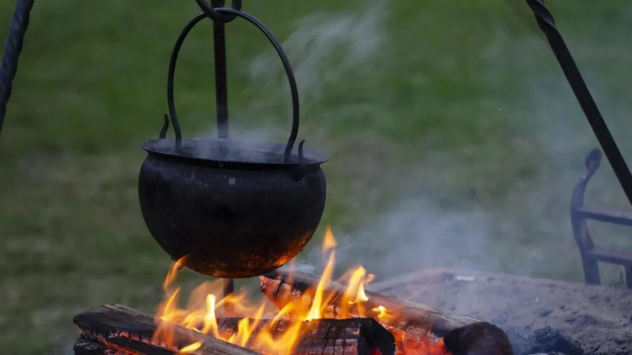Cast iron pot heating over open campfire flames with glowing coals in natural outdoor setting