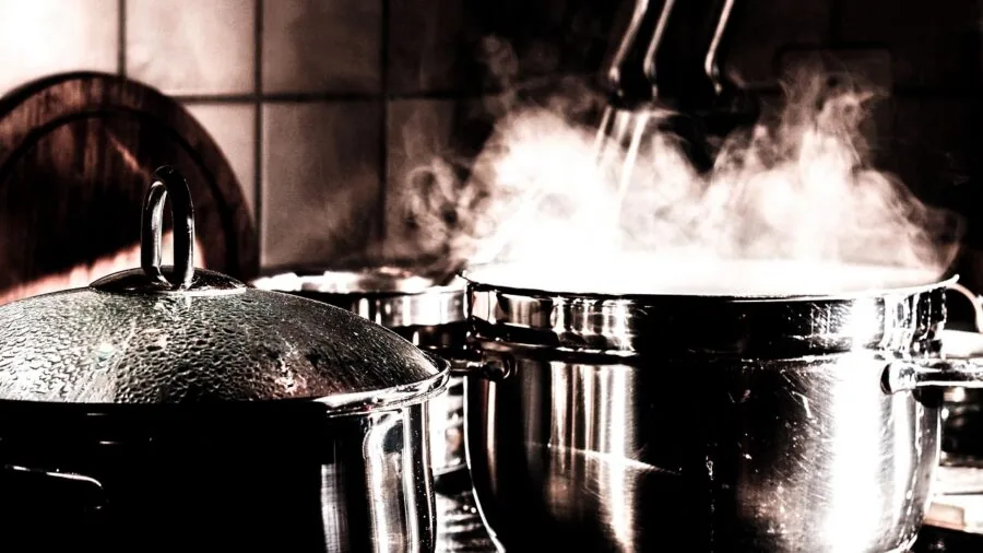 Chef lifting lid off pot releasing steam during braising, showing condensation and self-basting technique in kitchen