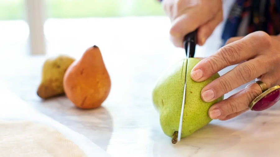 Chef's hands demonstrating precise knife technique while slicing fresh vegetables on a cutting board