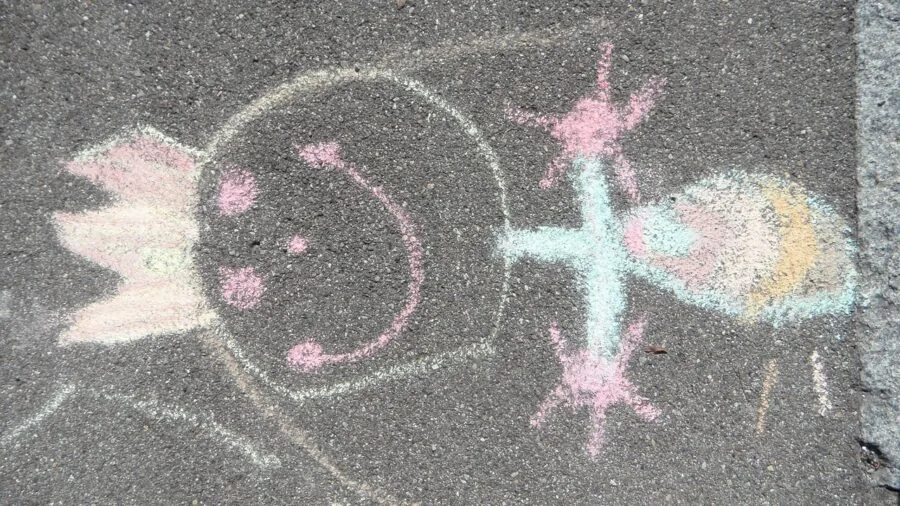 Child creating vibrant sidewalk chalk art on pavement, showing value and creative use of quality materials