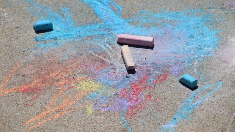 Child drawing with sidewalk chalk on pavement outside on sunny day