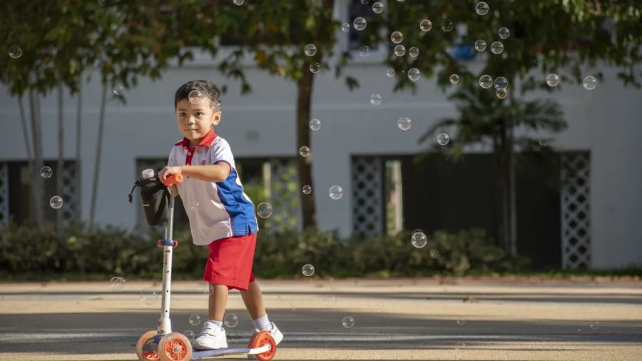 Child holding a compact folded scooter while walking outdoors in natural daylight