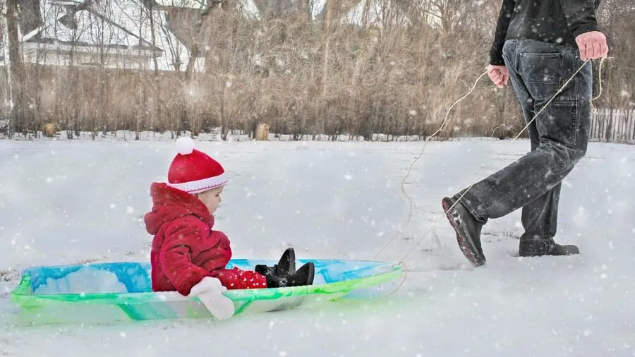 Child holding sled handles while sledding down snowy hill in winter