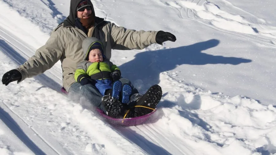 Child leaning into turn while sledding down snowy slope, demonstrating body weight steering technique