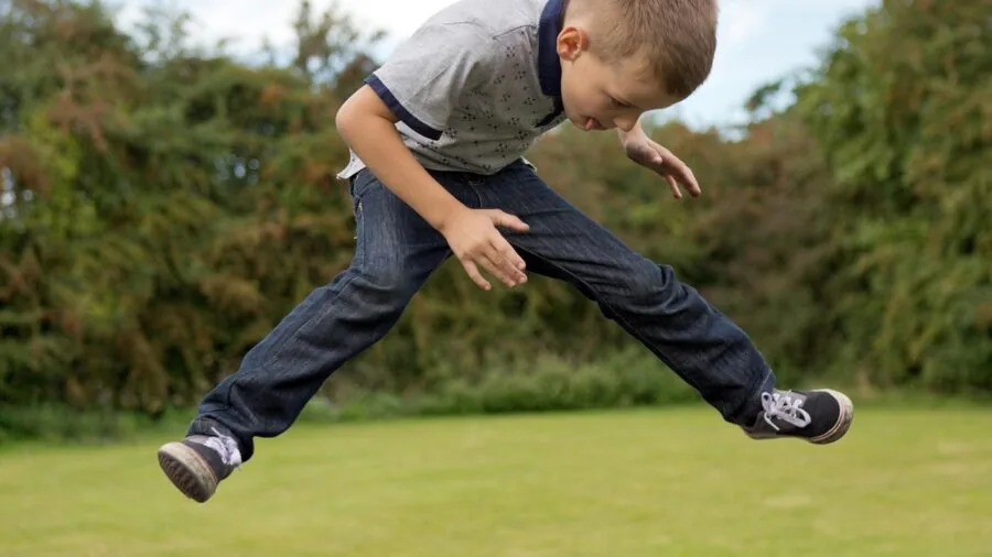 Child mid-jump on backyard trampoline during sunny day, capturing active outdoor play and dynamic movement