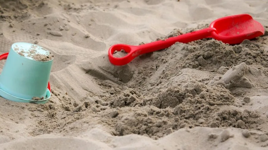 Child playing in wooden sandbox in sunny backyard during daytime