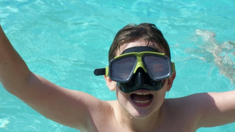 Child practicing swimming kicks in pool during swim lesson with instructor guidance