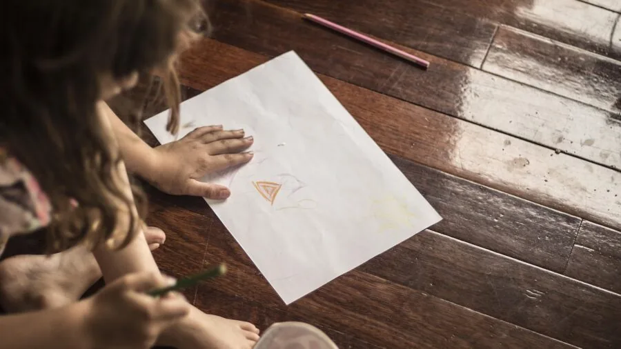 Child sketching with colored pencils on paper in natural light