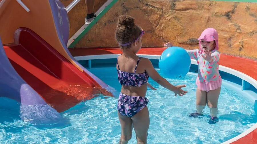 Children sliding down a colorful water slide on a sunny day with inflatable boards