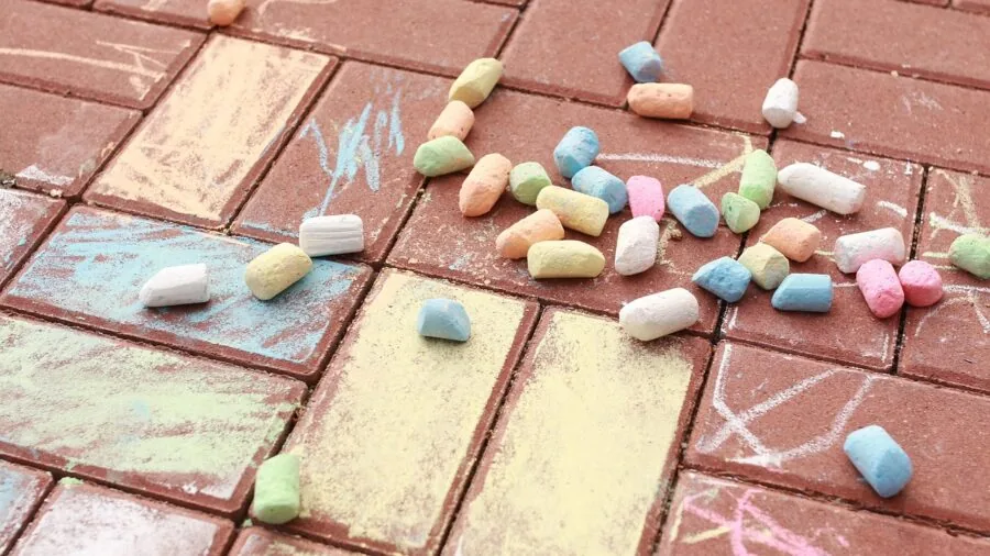 Child's hand holding broken chalk piece over colorful sidewalk drawing