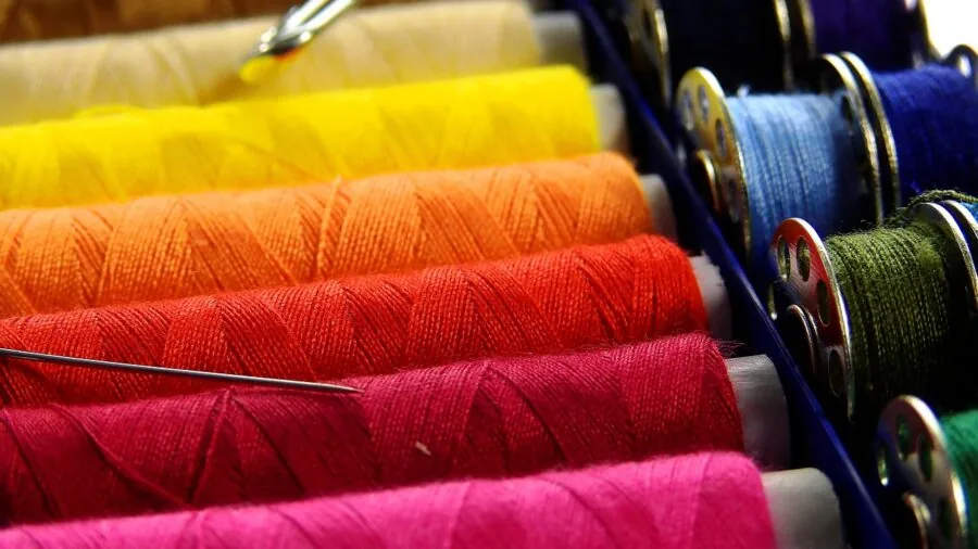 Child's hands arranging colorful thread, needles, and fabric pieces for a sewing project