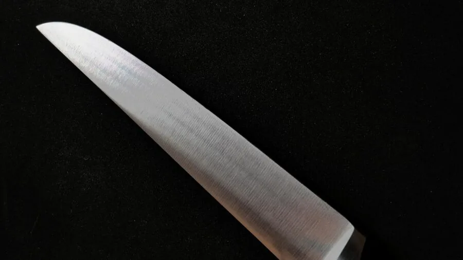 Close-up of a chef inspecting a high-quality kitchen knife blade under natural light