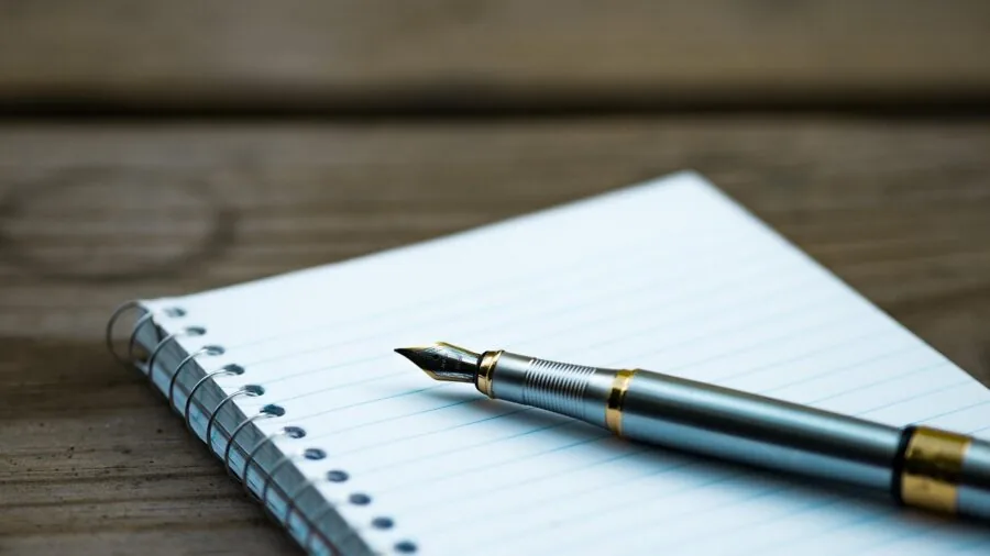 Close-up of a hand writing on white paper with a pen, showing ink application and drying on paper surface