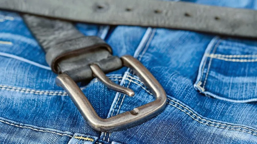 Close-up of a man fastening his leather belt buckle while getting dressed