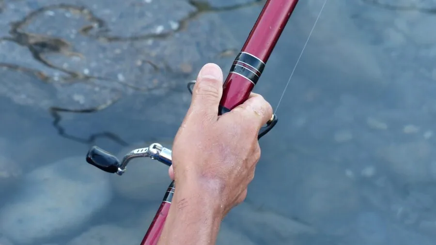 Close-up of angler's hands with strong grip on wet fishing rod during catch
