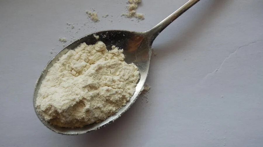 Close-up of baker measuring flour and ingredients while preparing dough in a home kitchen