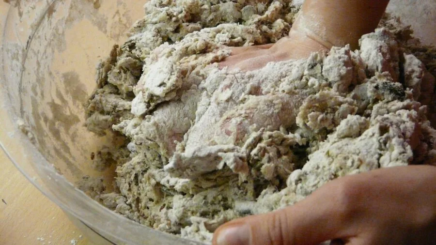 Close-up of baker's hands kneading dough on wooden surface during baking session