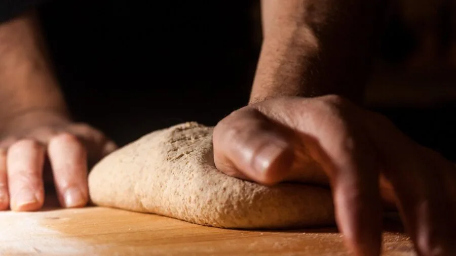 Close-up of baker's hands working with dough on a baking surface, showing texture and technique