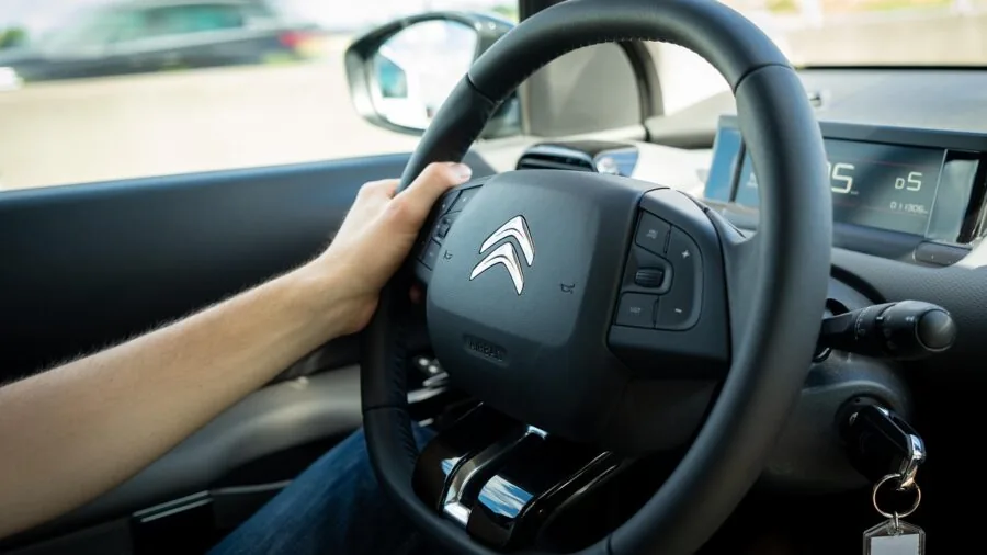 Close-up of driver's hands gripping steering wheel while driving on road